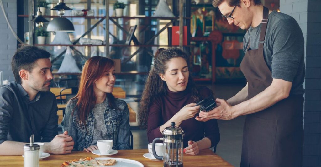 Group of friends having coffee and paying with card in a cozy café setting.