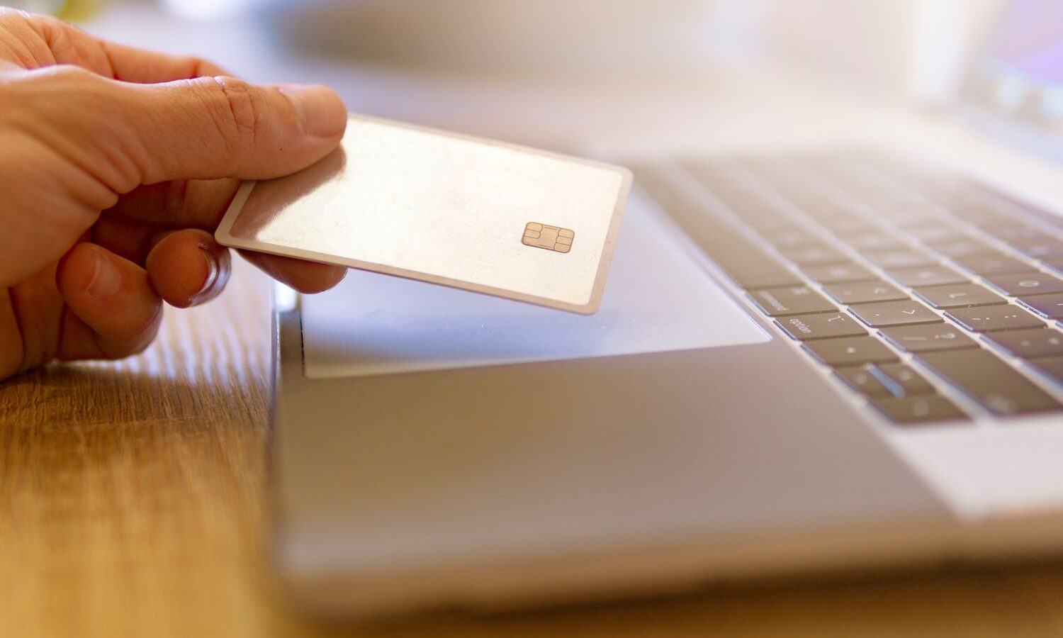 Mão segurando um cartão branco sobre um notebook