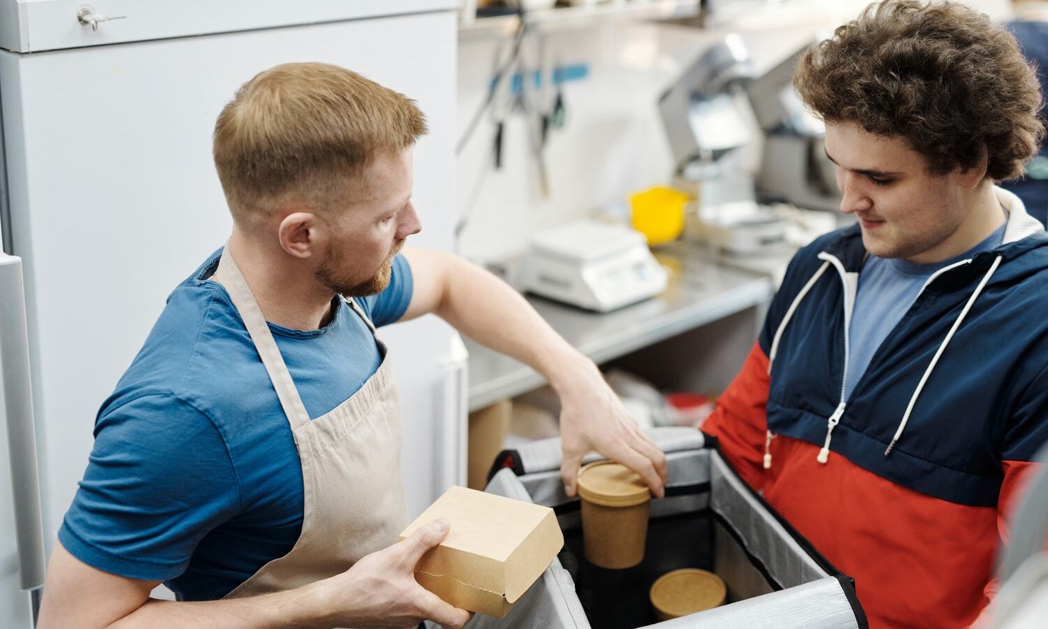 Entregador recebendo pedido de delivery embalado na cozinha do restaurante
